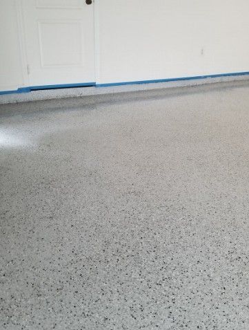 Speckled gray garage floor with white double doors and blue painter’s tape along the baseboard