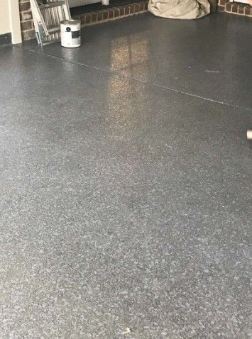 Speckled dark-gray floor in an indoor space with a small white can and beige bag in the background