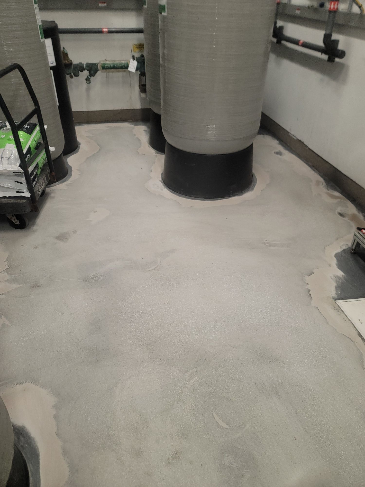 Basement utility room with a concrete floor and large cylindrical column, wet or freshly coated floor visible.