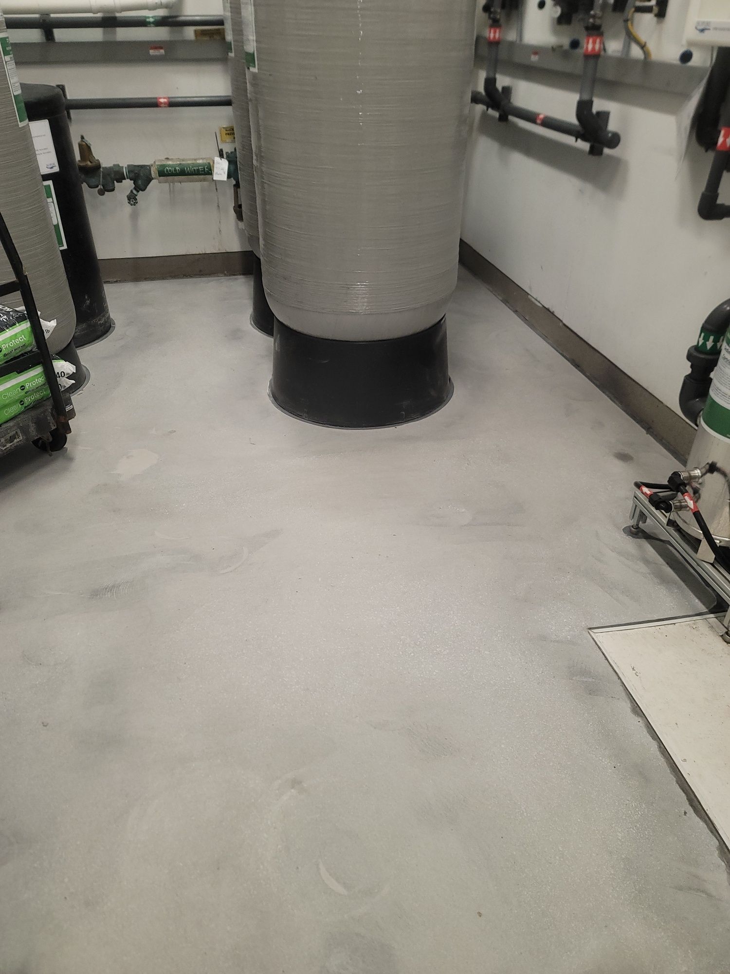 Utility room with a large central duct, pipes along the walls, and a gray concrete floor.