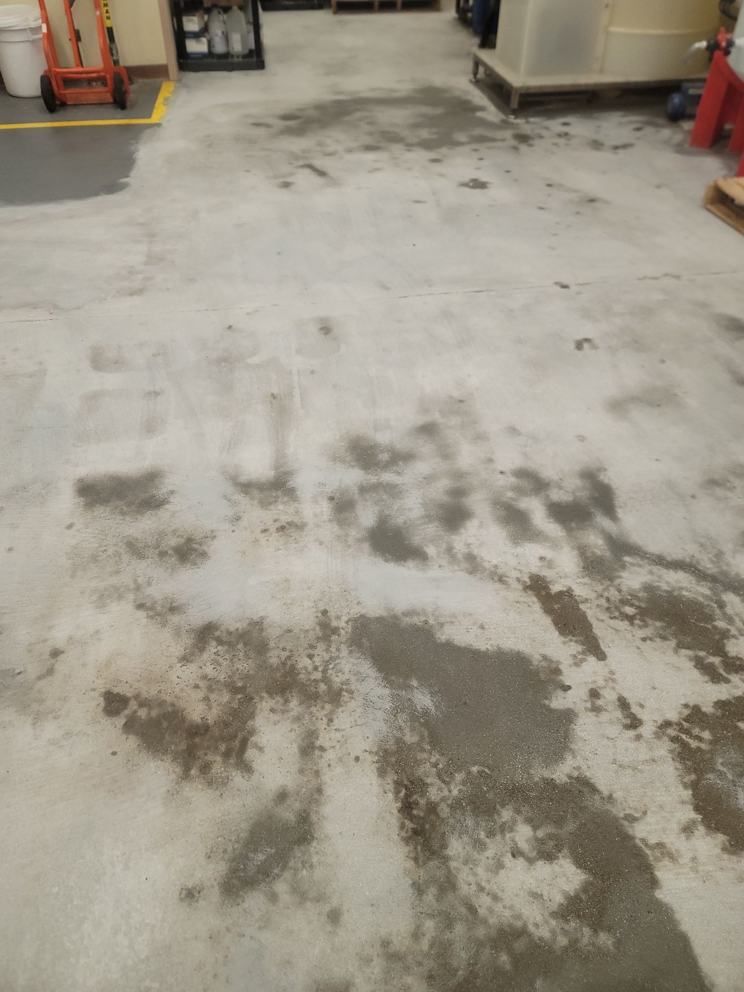 Dirty concrete floor in a garage or workshop with dark stains and scattered debris.
