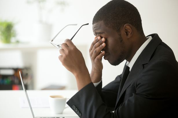 A man in a suit is rubbing his eyes while sitting in front of a laptop computer.