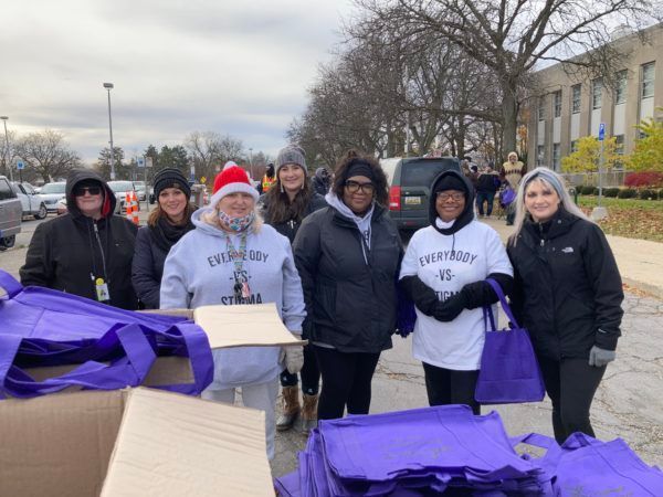 A group of women are standing in front of purple bags and boxes.