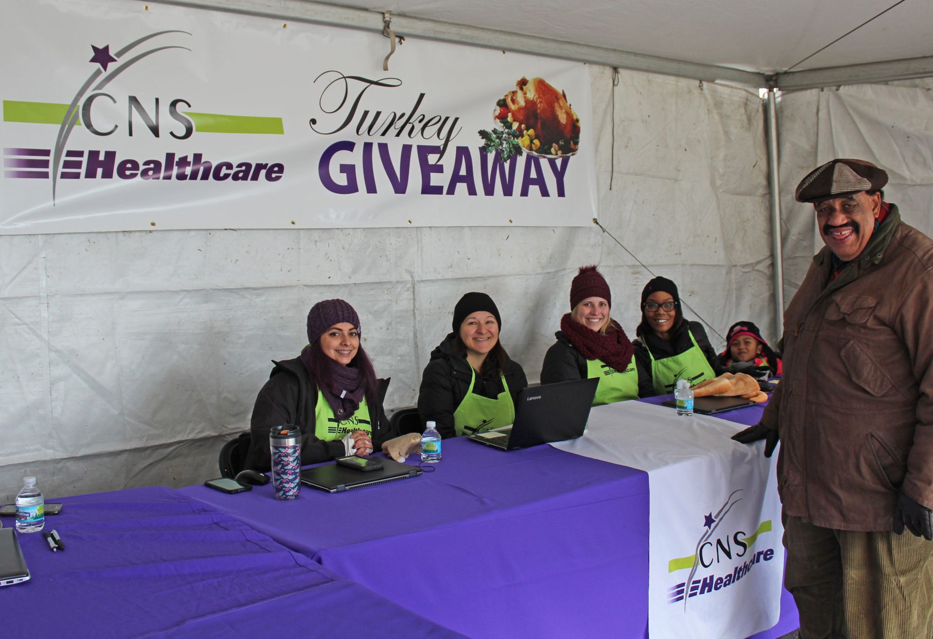 A group of people sitting at a table under a banner that says cns healthcare turkey giveaway