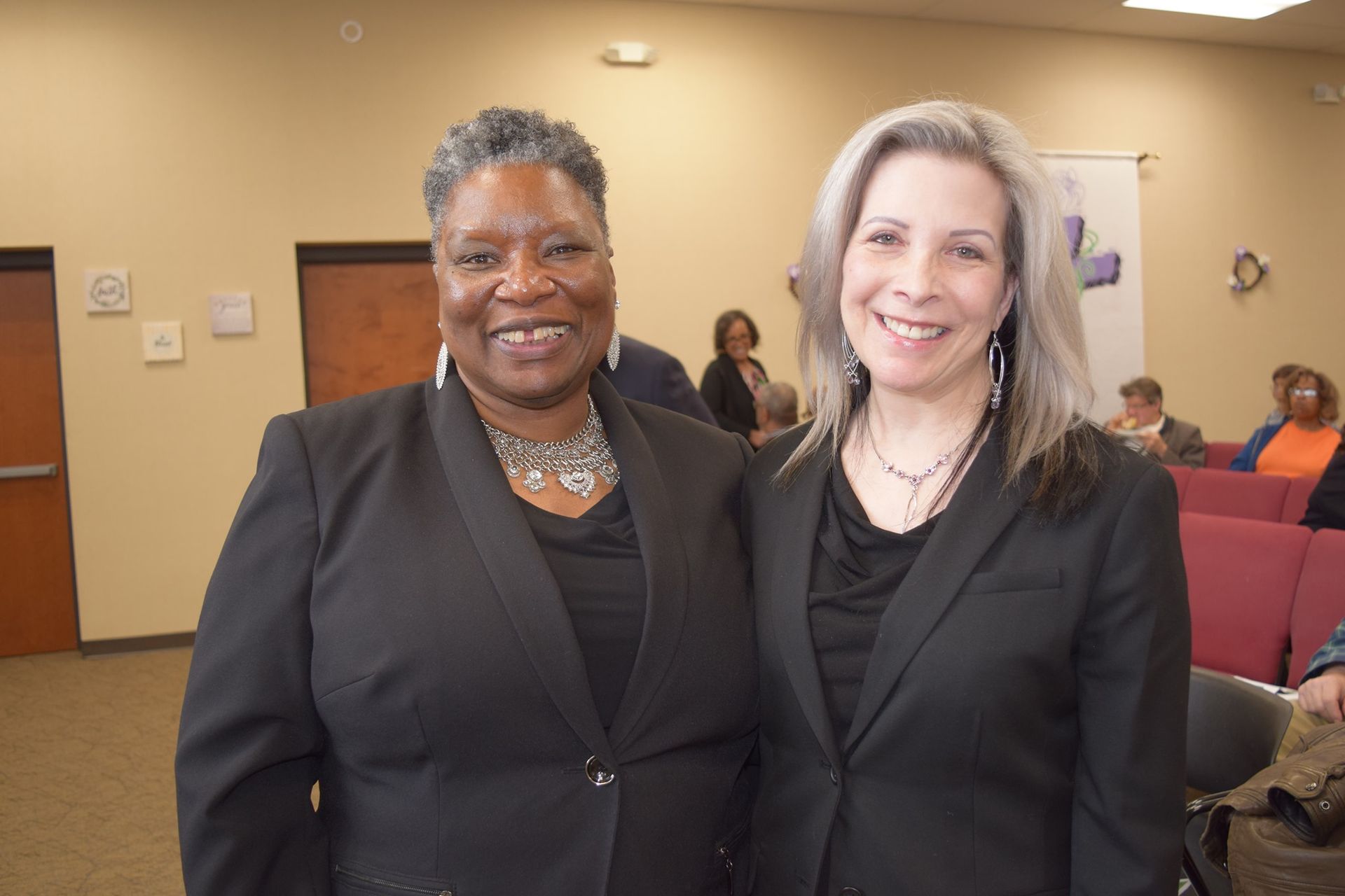 Two women in suits are posing for a picture in a room.