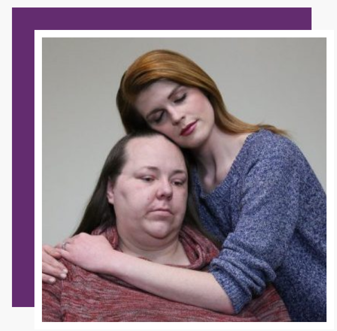 A woman in a blue sweater is hugging another woman