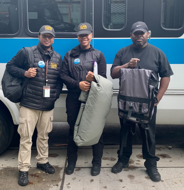 Three people standing in front of a bus with one wearing a hat that says ucsd