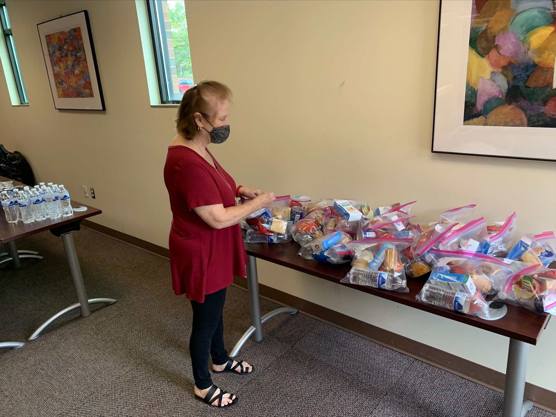 A woman wearing a mask is standing in front of a table filled with bags of food.