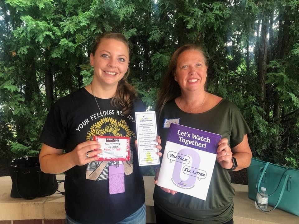 Two women are standing next to each other holding a booklet that says let 's watch together.