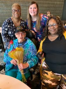 A group of people are posing for a picture while a man in a wheelchair is holding a bouquet of flowers.