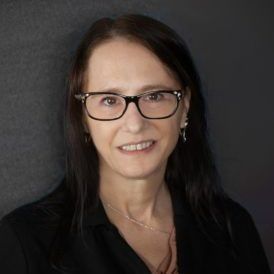 A woman wearing glasses and a black shirt is smiling for the camera.