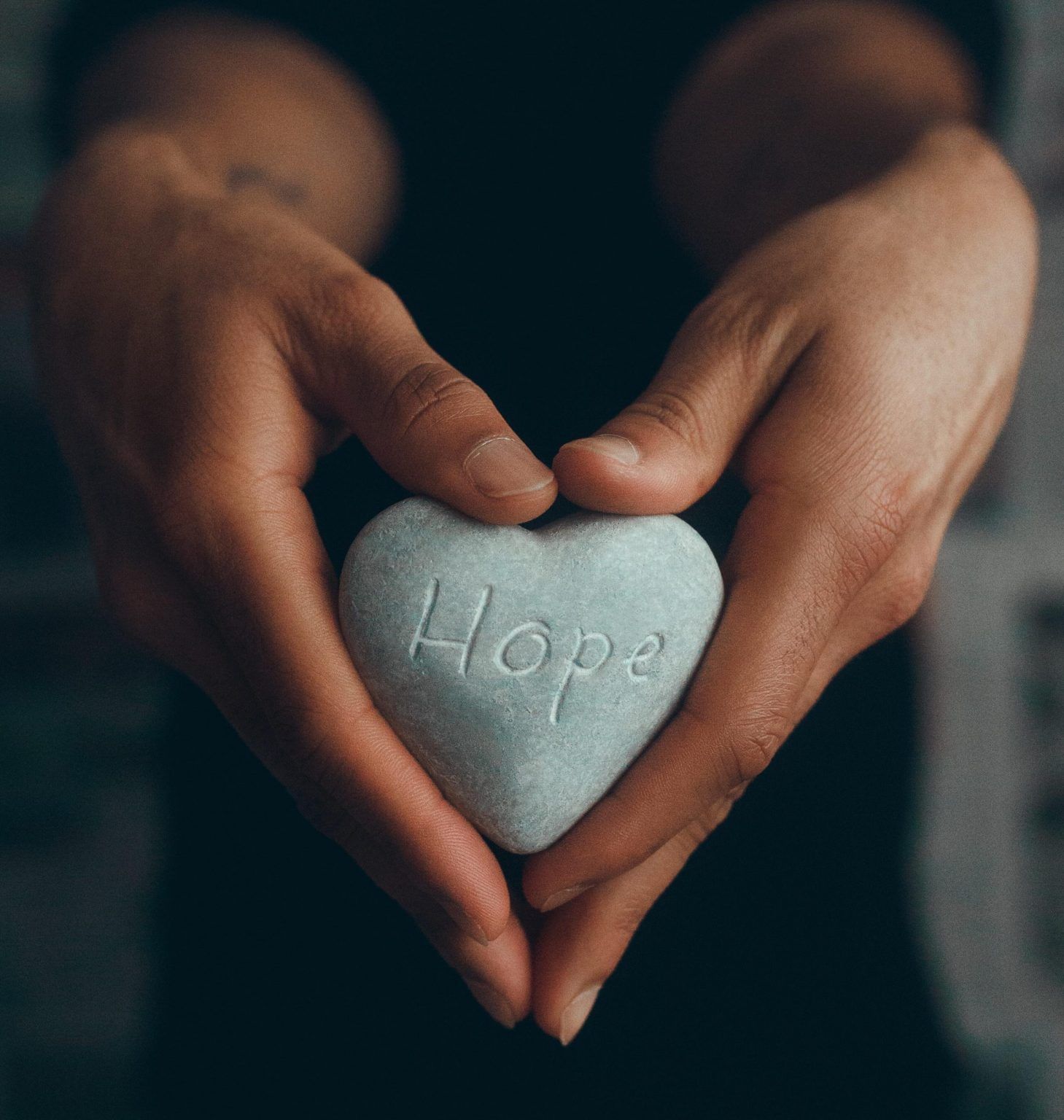 A person is holding a heart shaped rock with the word hope carved into it.