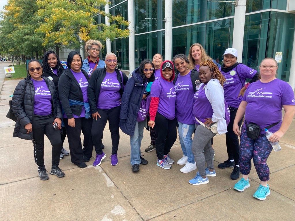 A group of women wearing purple CNS shirts are posing for a picture.