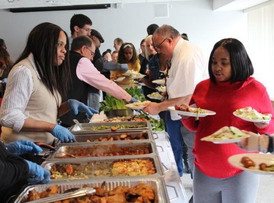 A woman in a red sweater is getting food from a buffet line