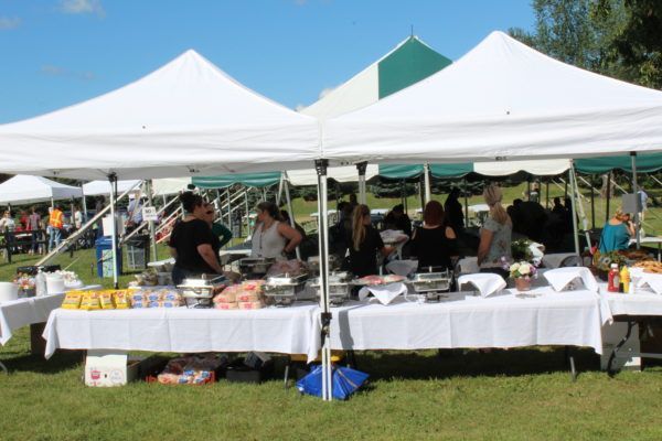 A group of people are standing around tables under tents in a field.