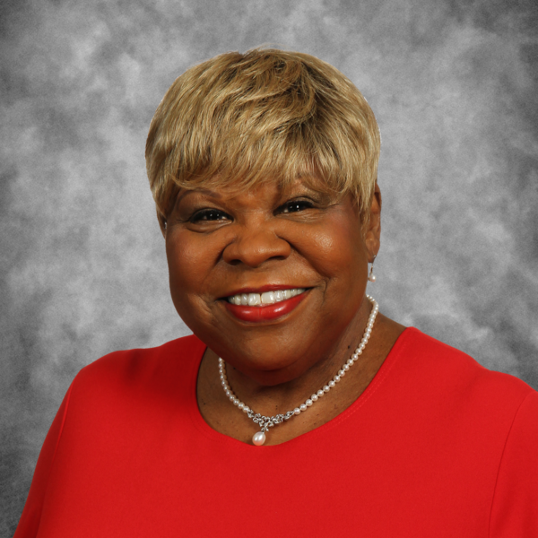 A woman wearing a red shirt and a pearl necklace smiles for the camera