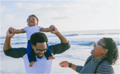 A man is carrying a baby on his shoulders on the beach.