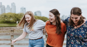 Three young women are walking across a bridge and laughing.