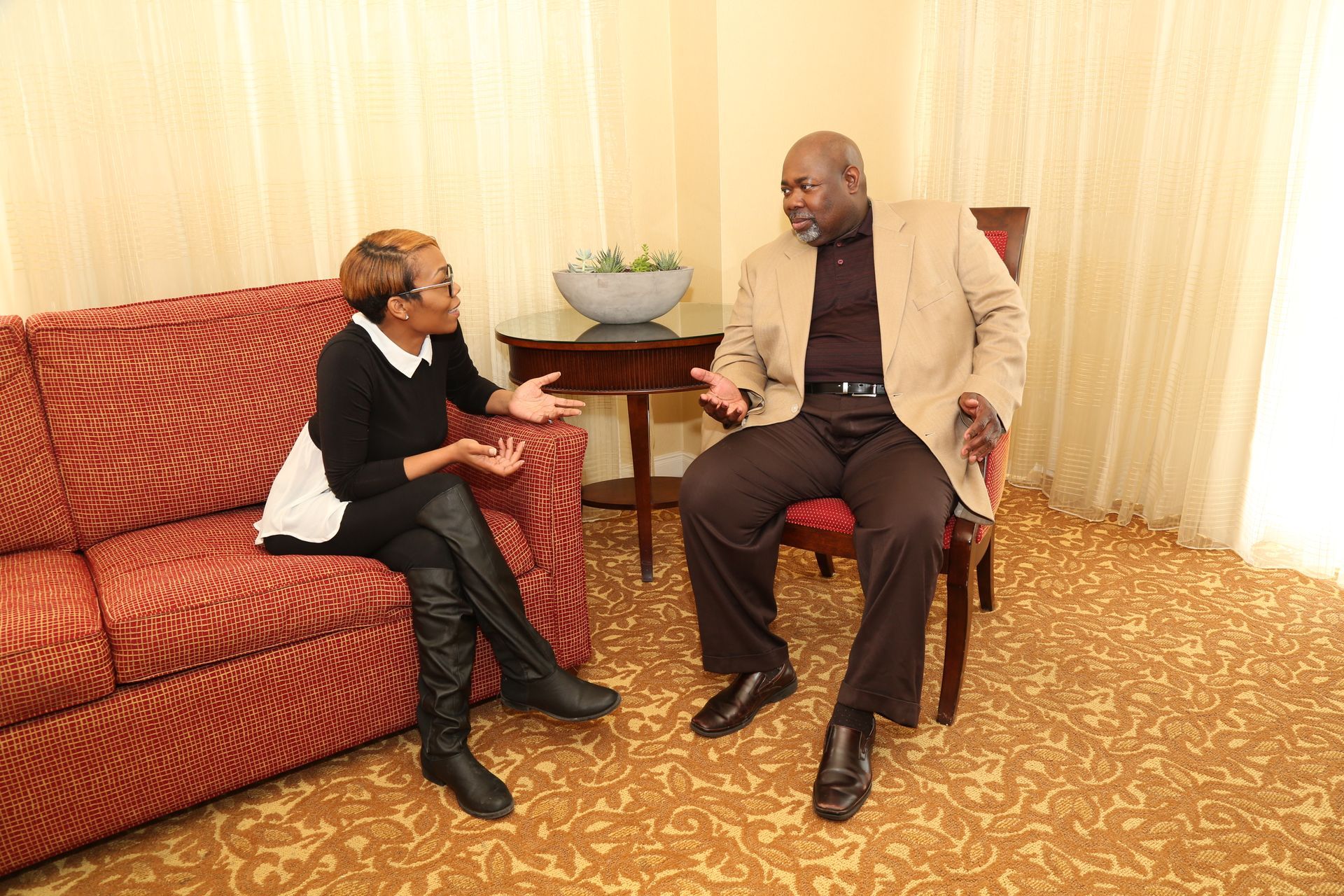 A man and a woman are sitting on a couch talking to each other.