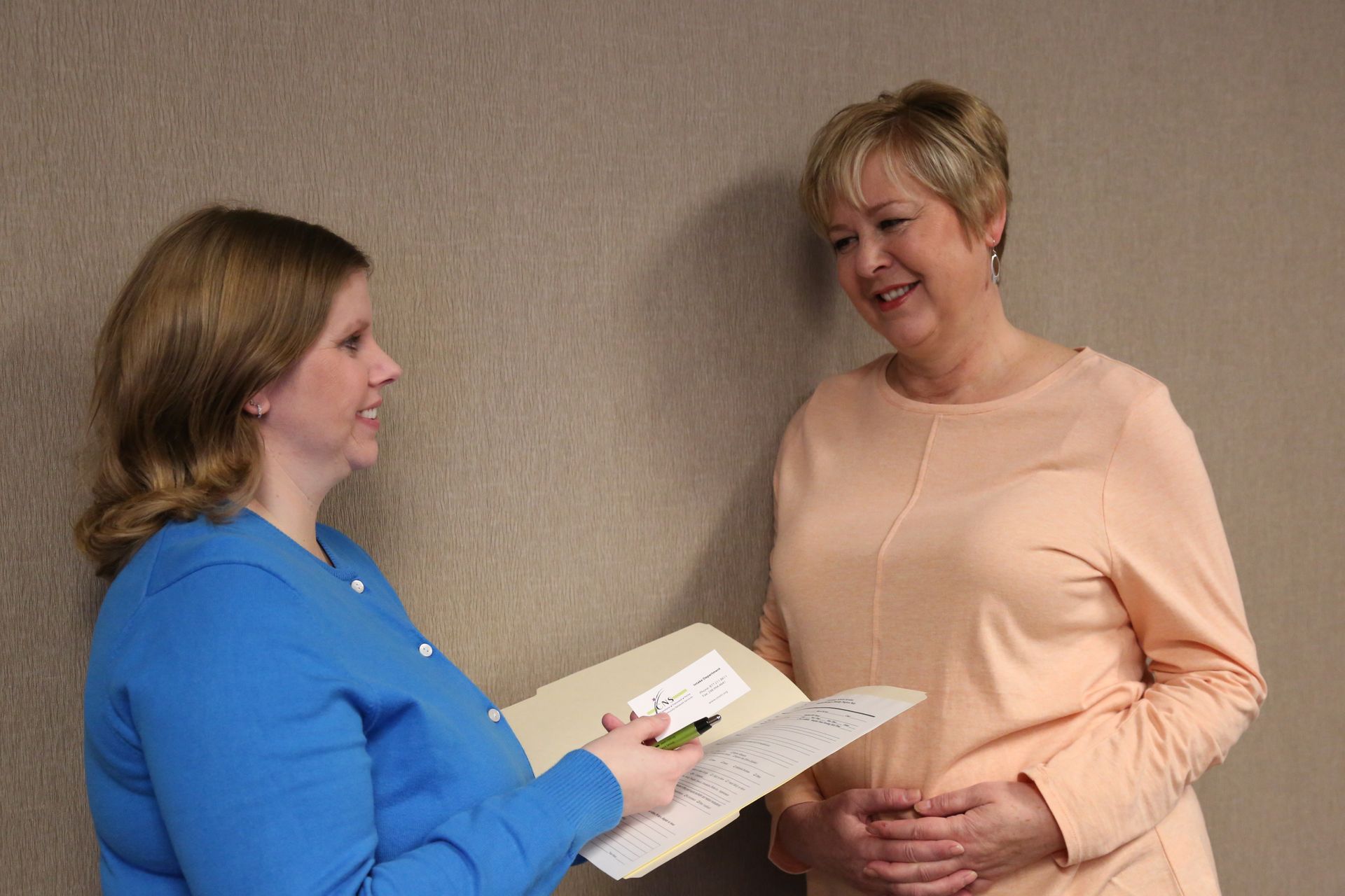 Two women are standing next to each other holding a clipboard and smiling.