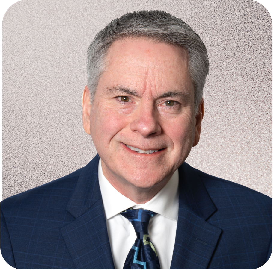 Man in blue suit smiling, wearing a patterned tie, against a neutral background.