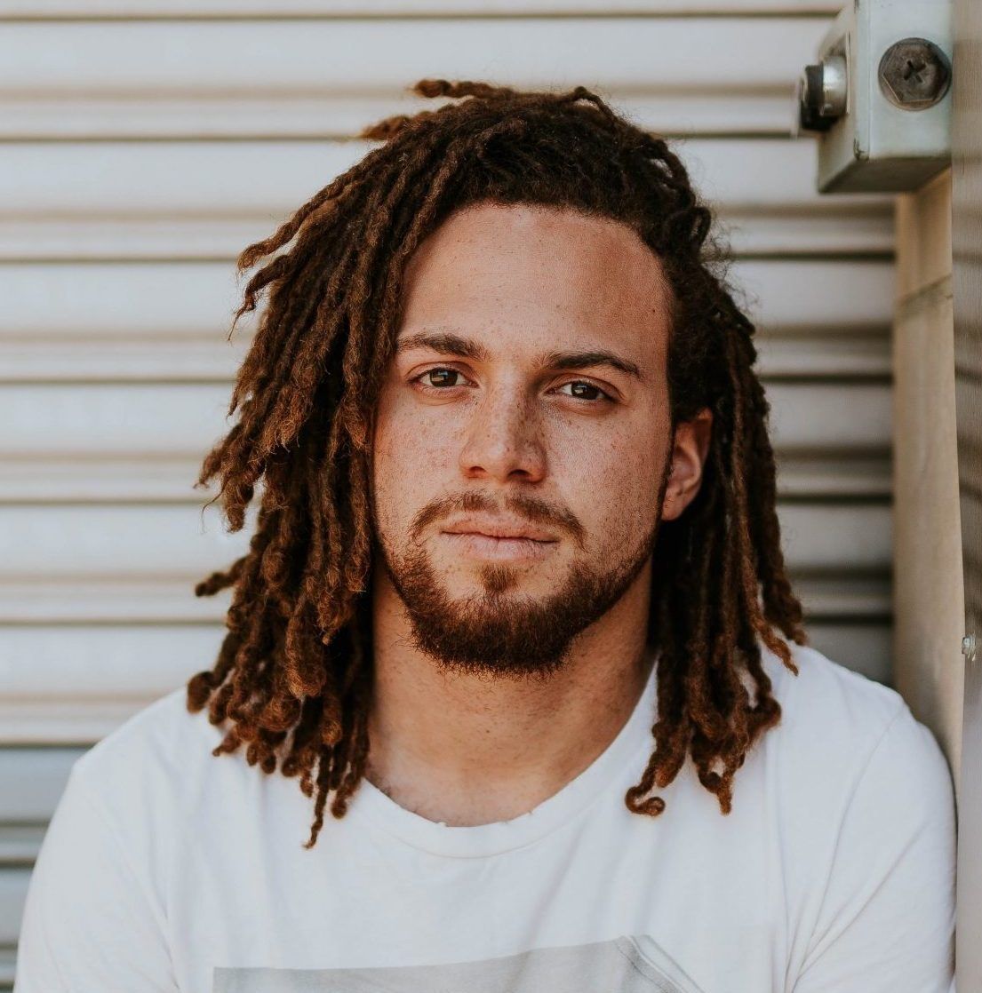 A man with dreadlocks and a beard is wearing a white shirt