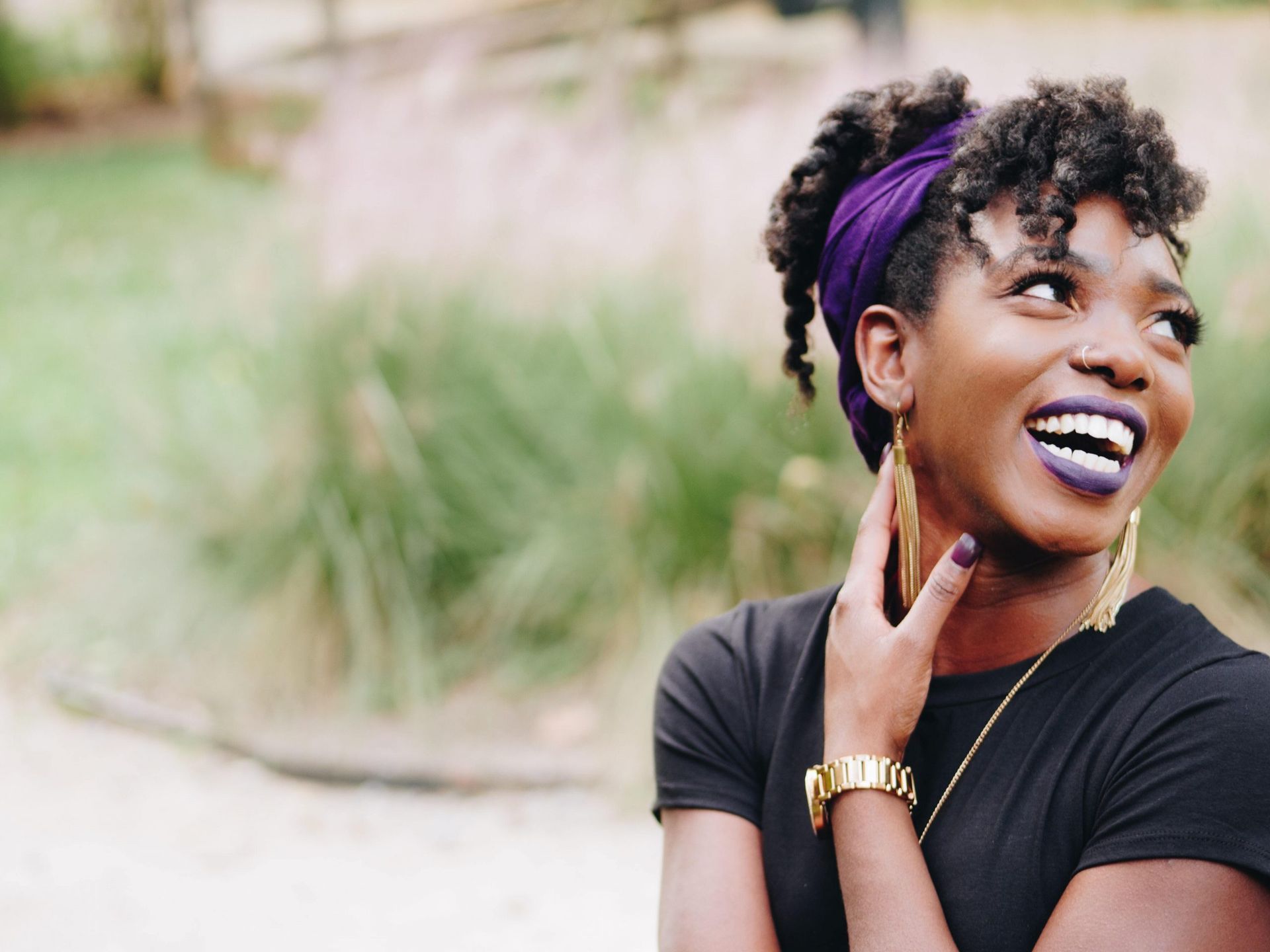 A woman wearing purple lipstick and a purple headband is smiling.