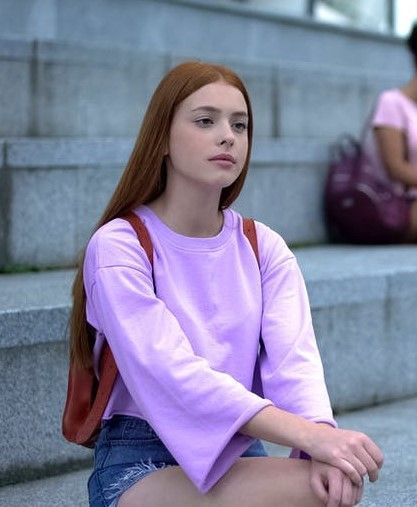 A young woman is sitting on a set of stairs wearing a purple sweater and shorts.