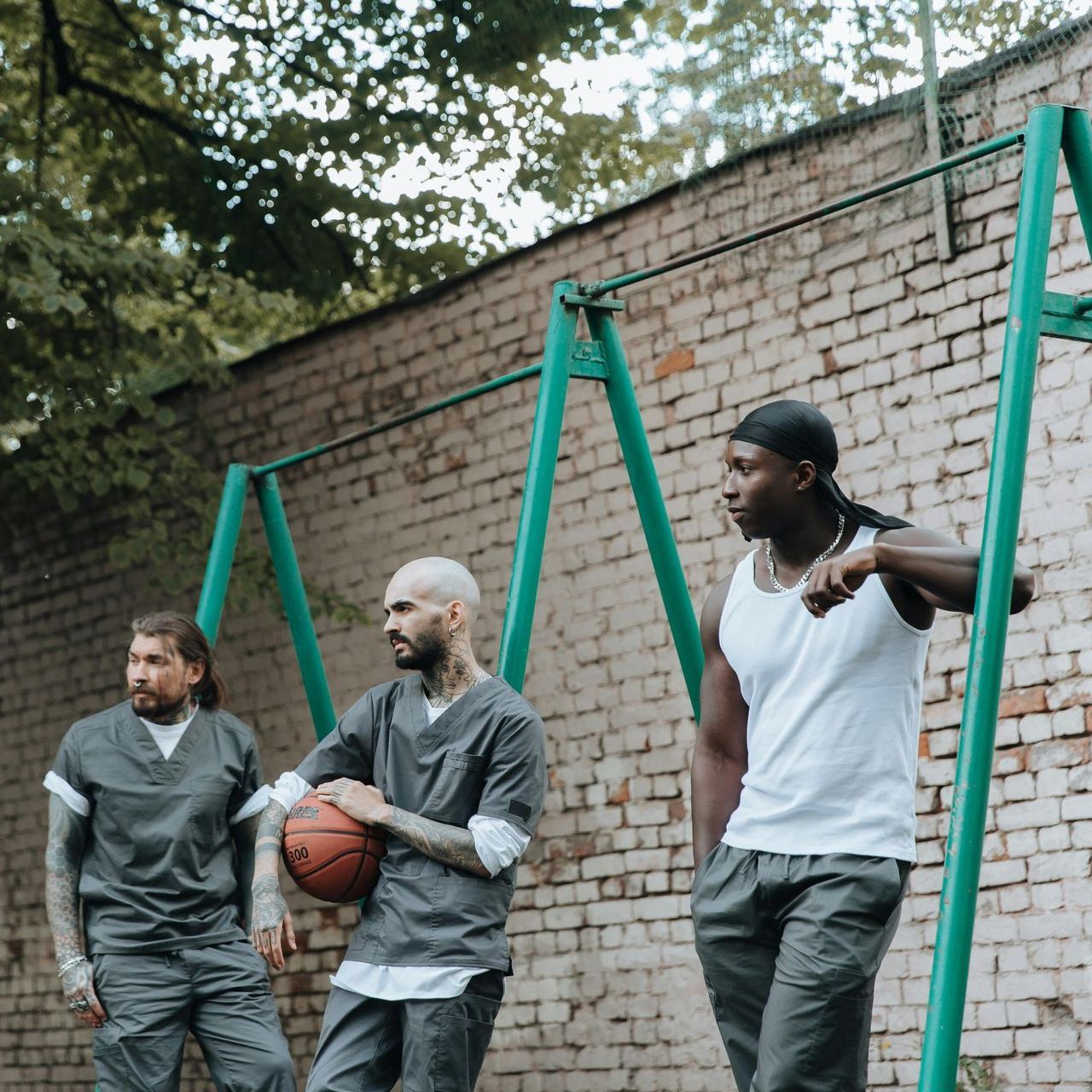 Three men are playing basketball in front of a brick wall