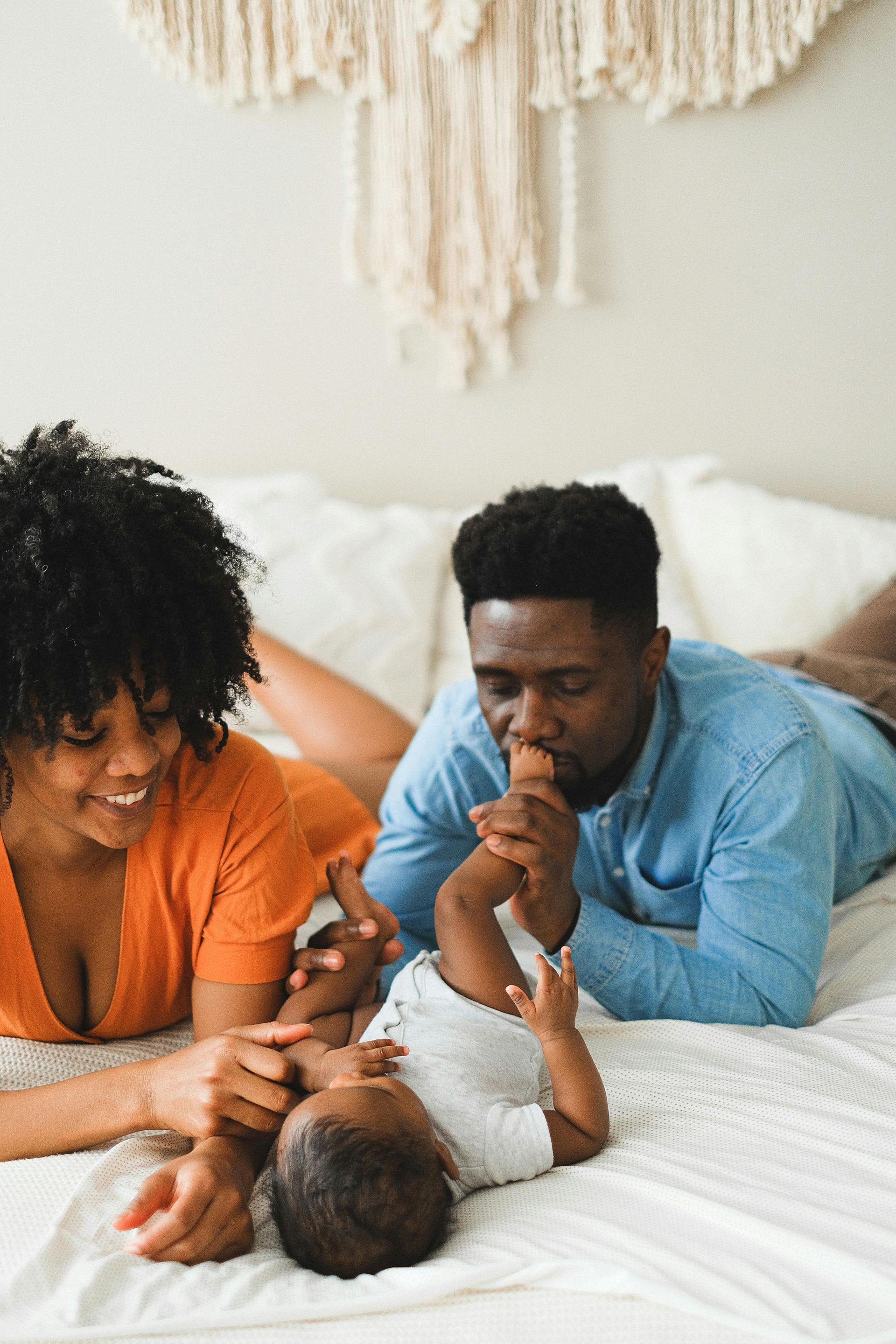 A man and woman are laying on a bed with a baby.