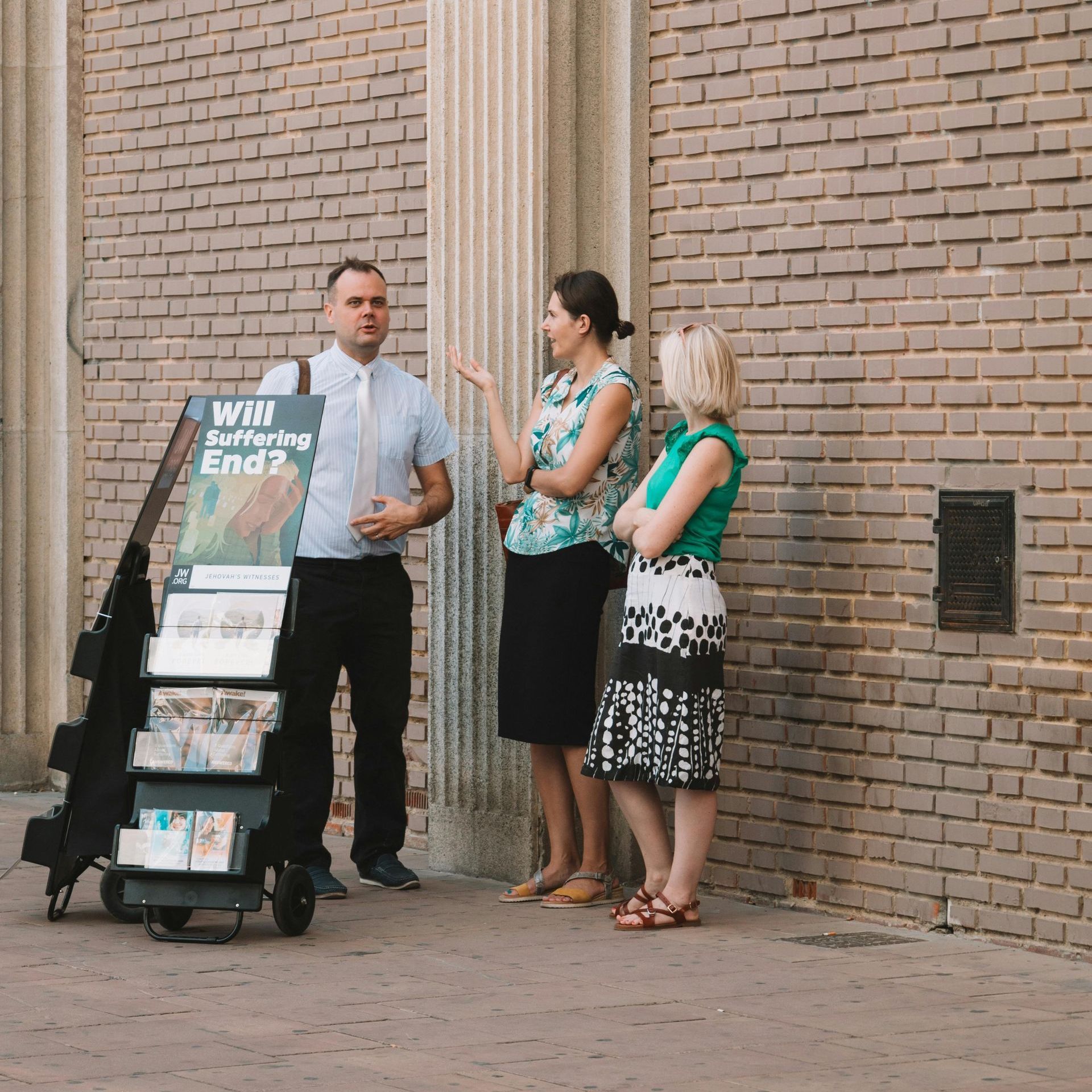 A man is talking to two women in front of a brick wall