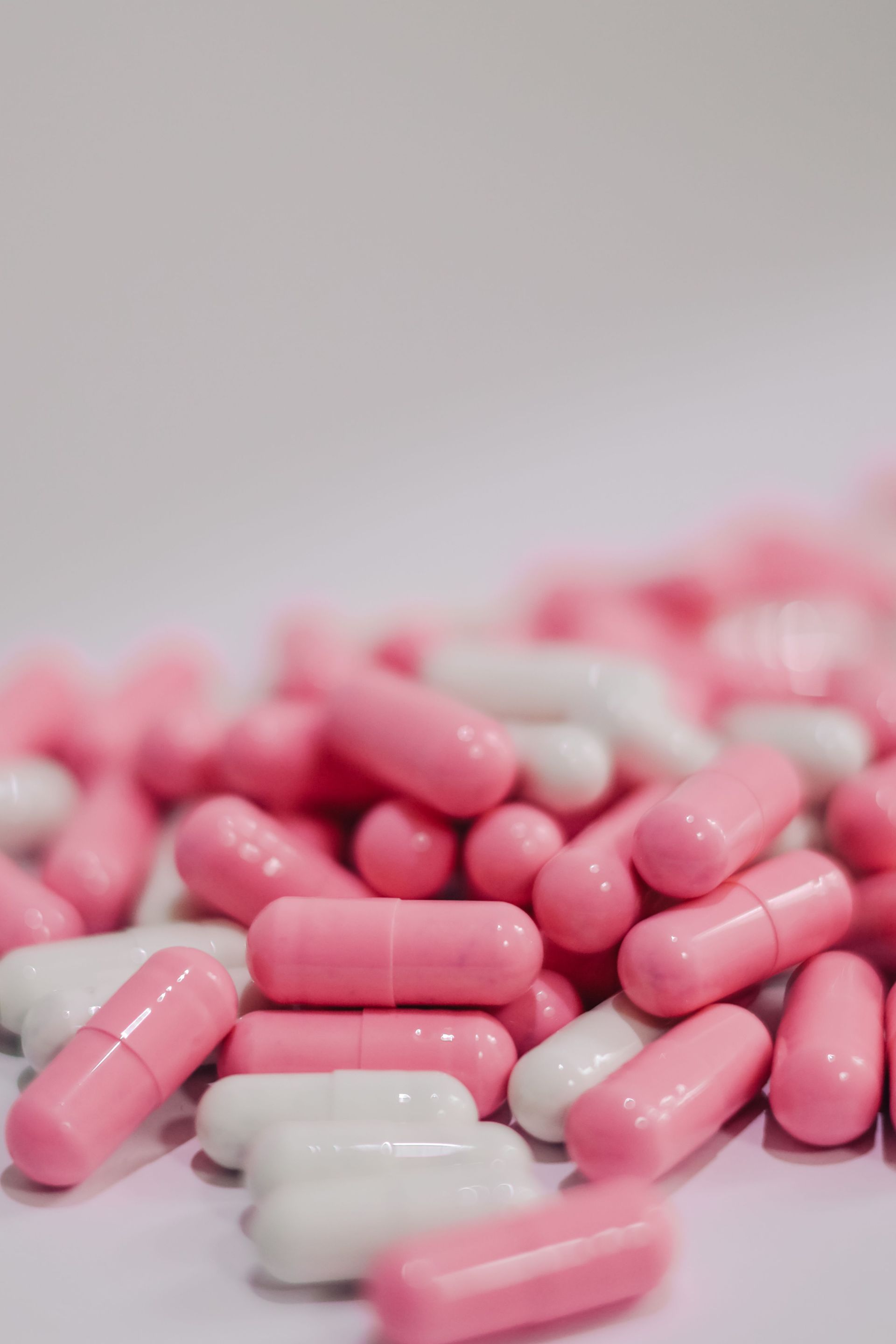 Pink and white capsules scattered on a white surface