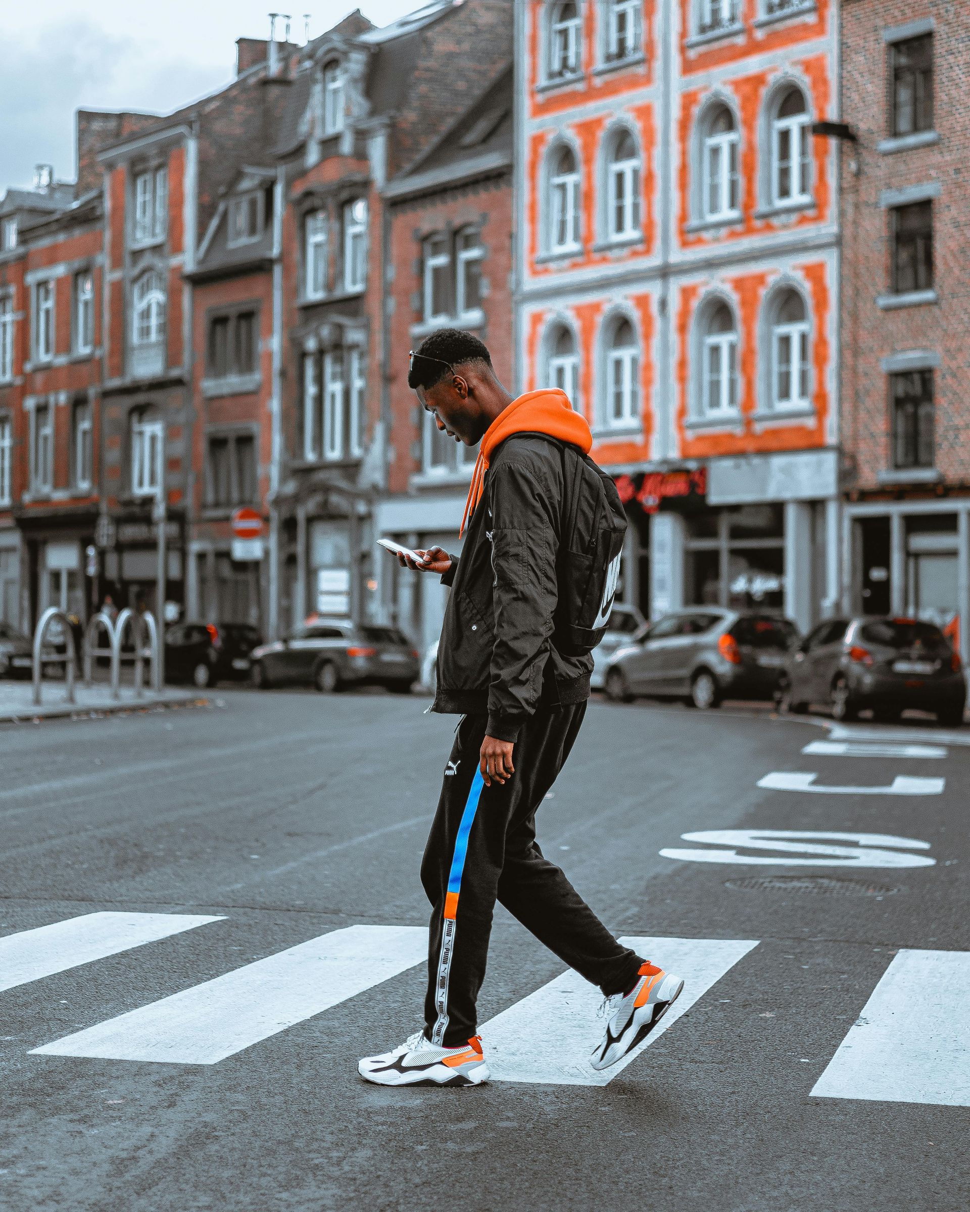 A man is crossing the street while looking at his phone.