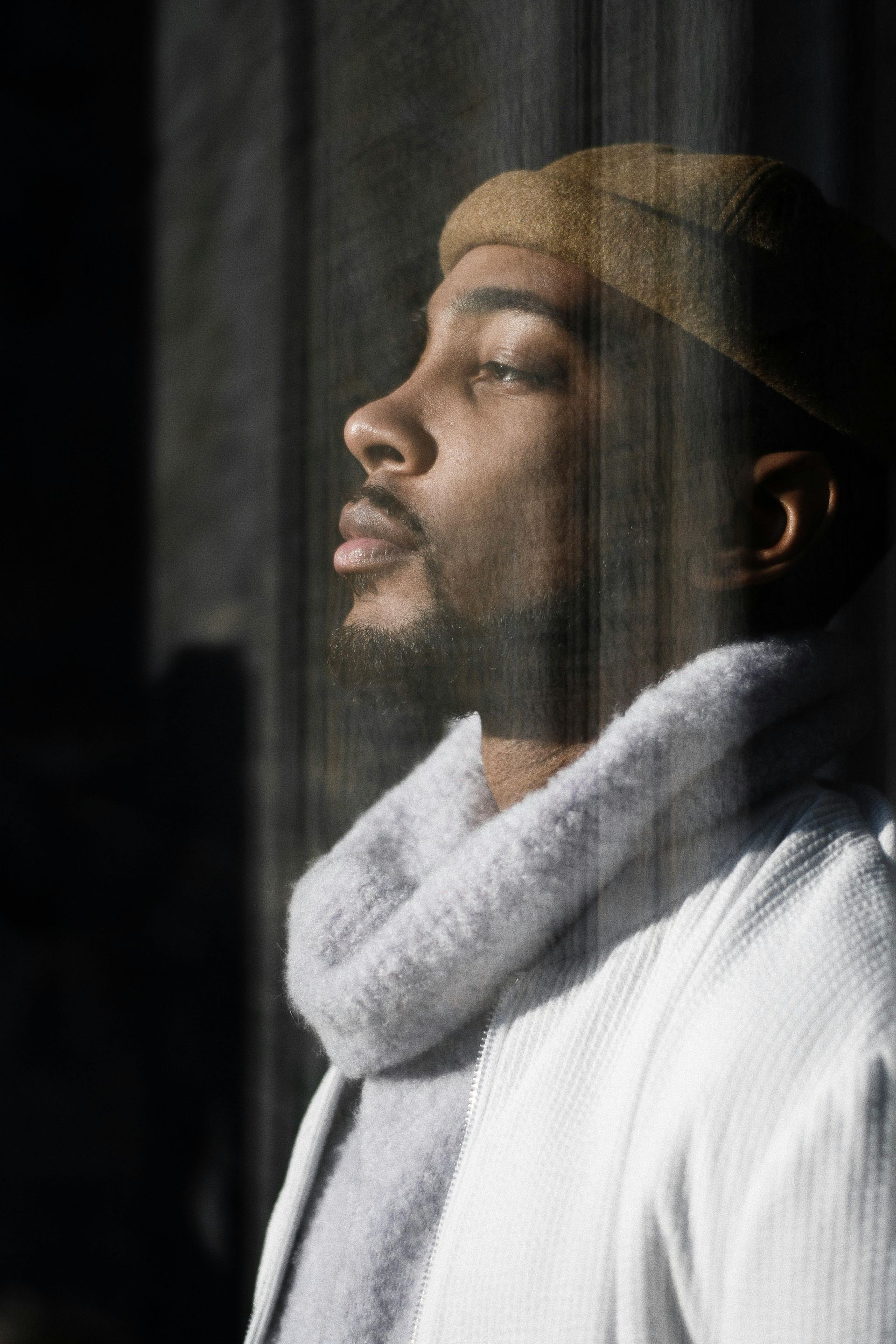 Man in a beanie and scarf, in profile, looking up towards sunlight.