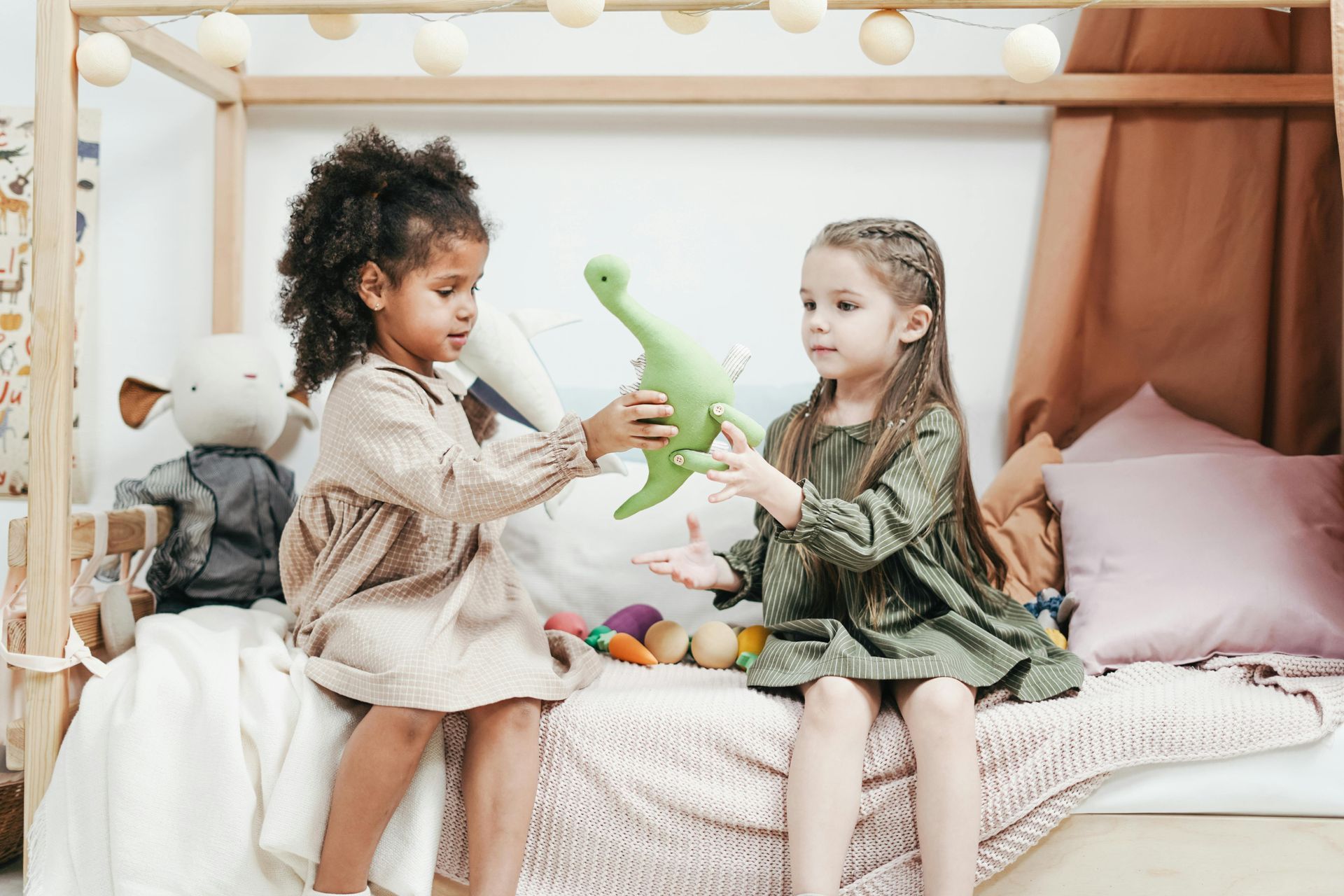 Two young girls sharing a green dinosaur toy in a classroom.