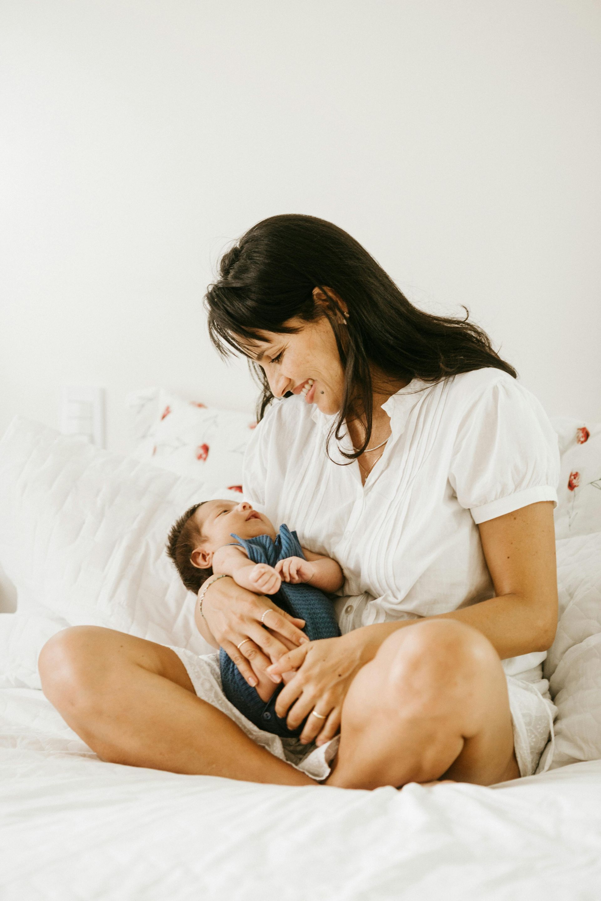 A woman is sitting on a bed holding a baby.