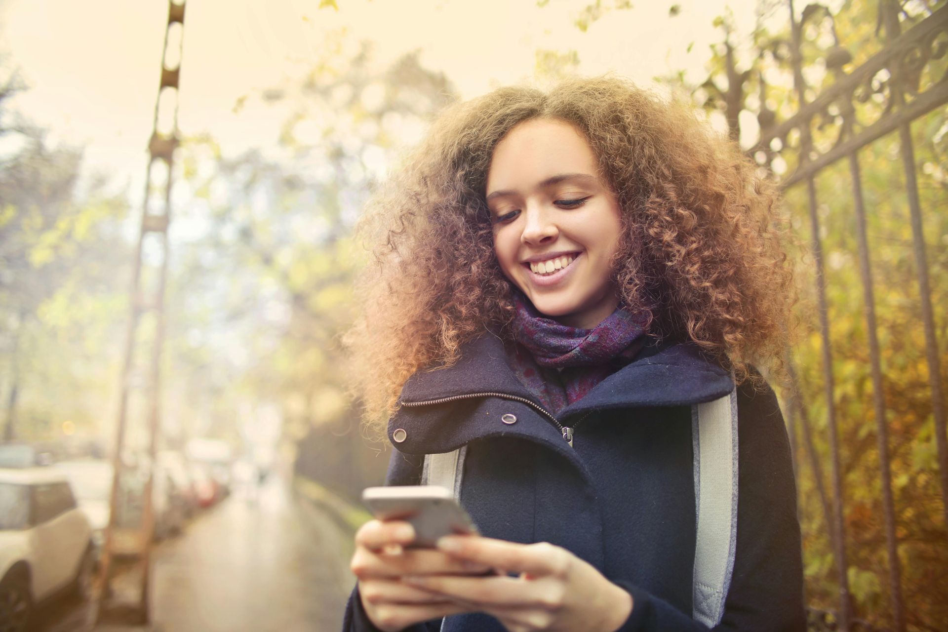 A woman is standing on a sidewalk looking at her cell phone.