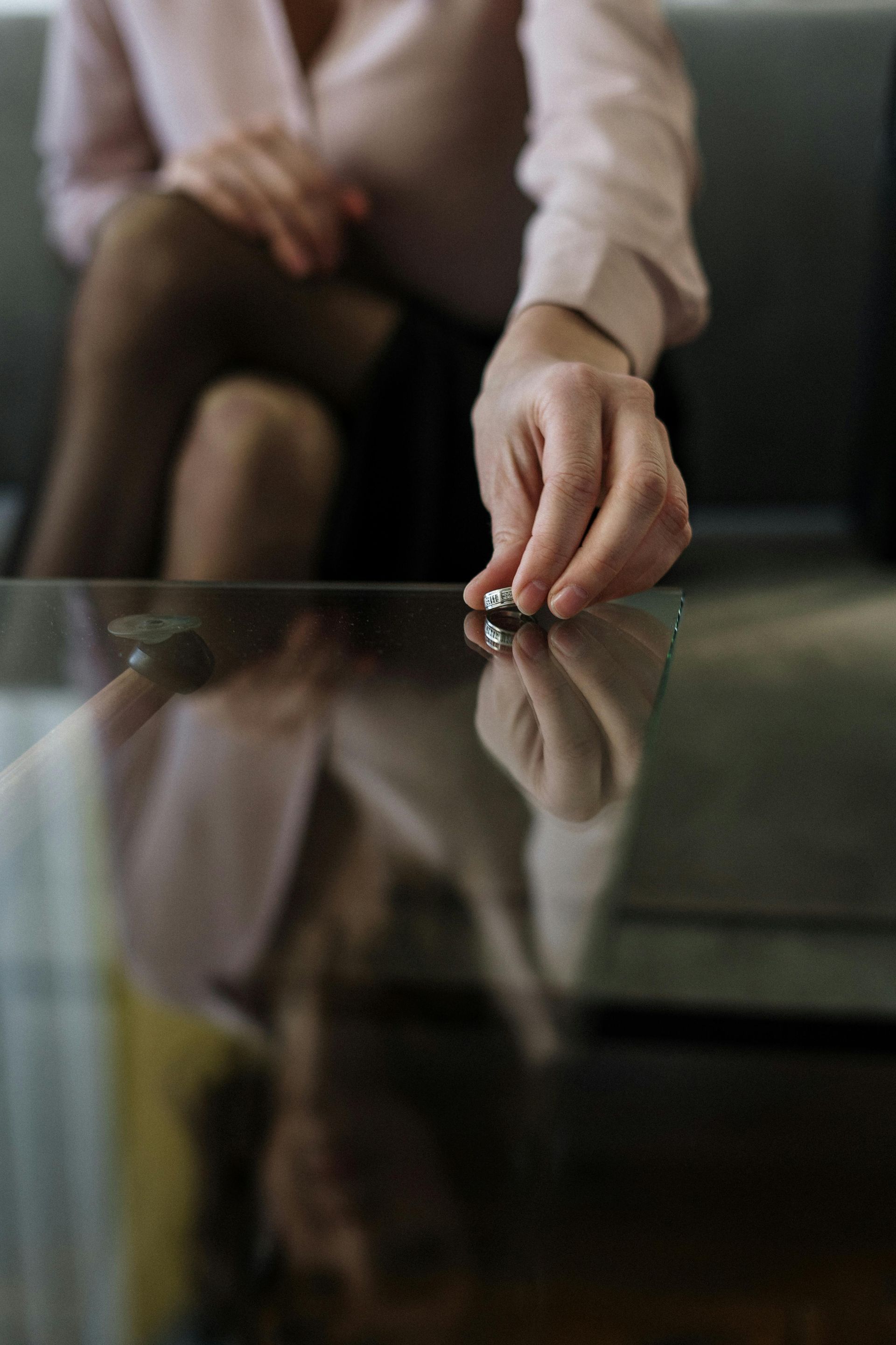 A woman is sitting on a couch holding a wedding ring on a glass table.