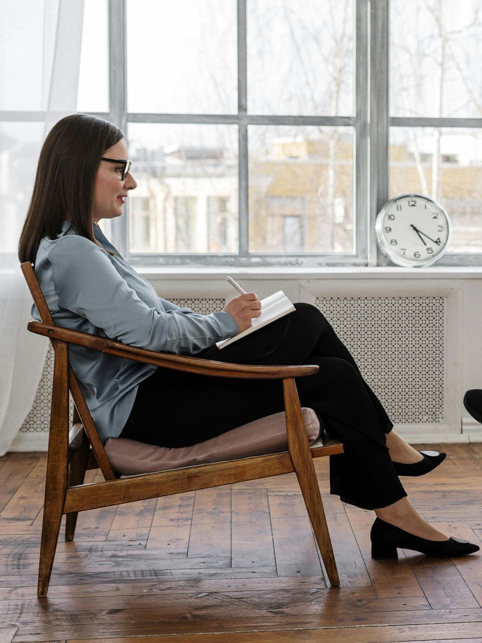 A woman is sitting in a chair writing in a notebook.