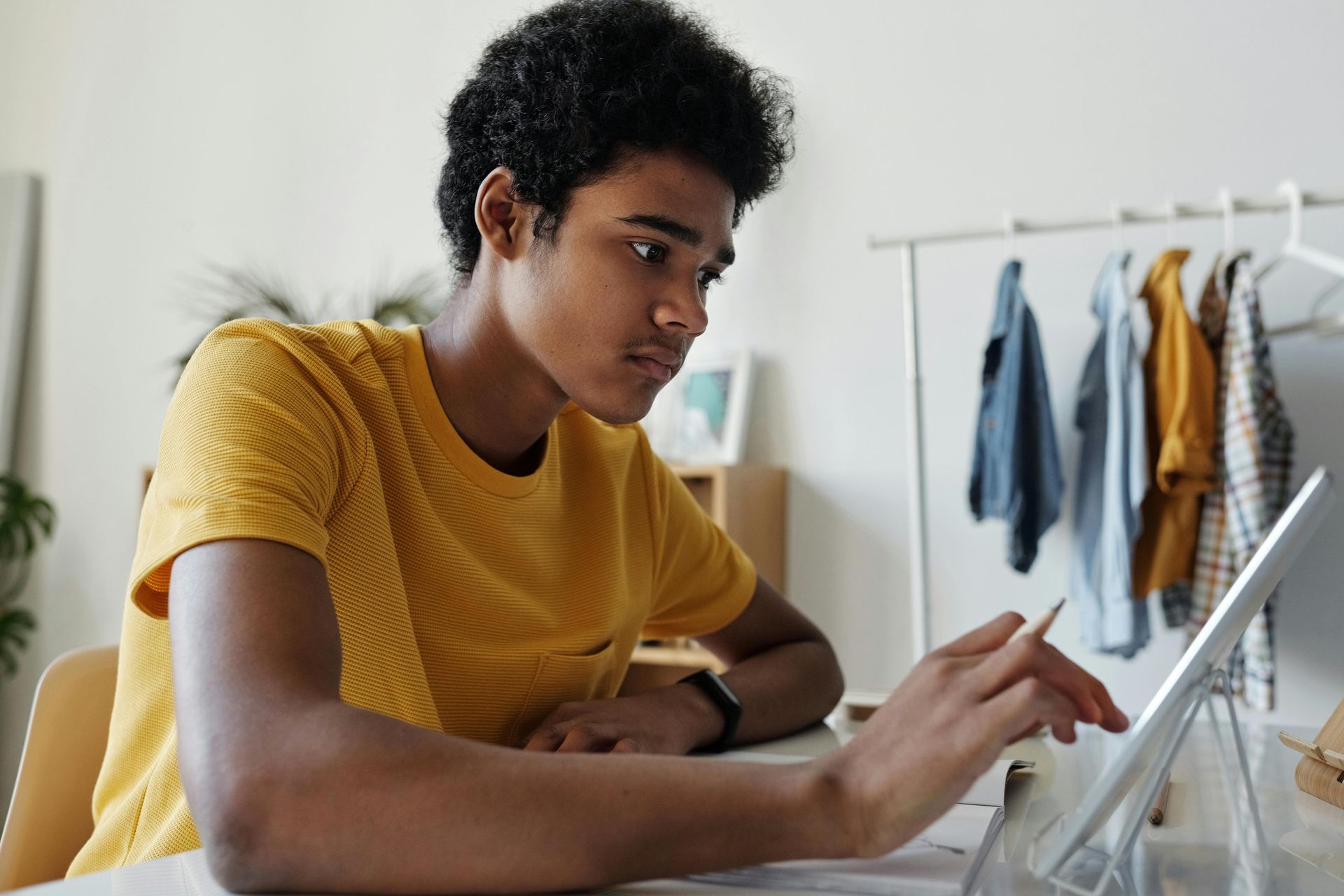 Teen with curly hair wearing yellow shirt, using a tablet at a table.