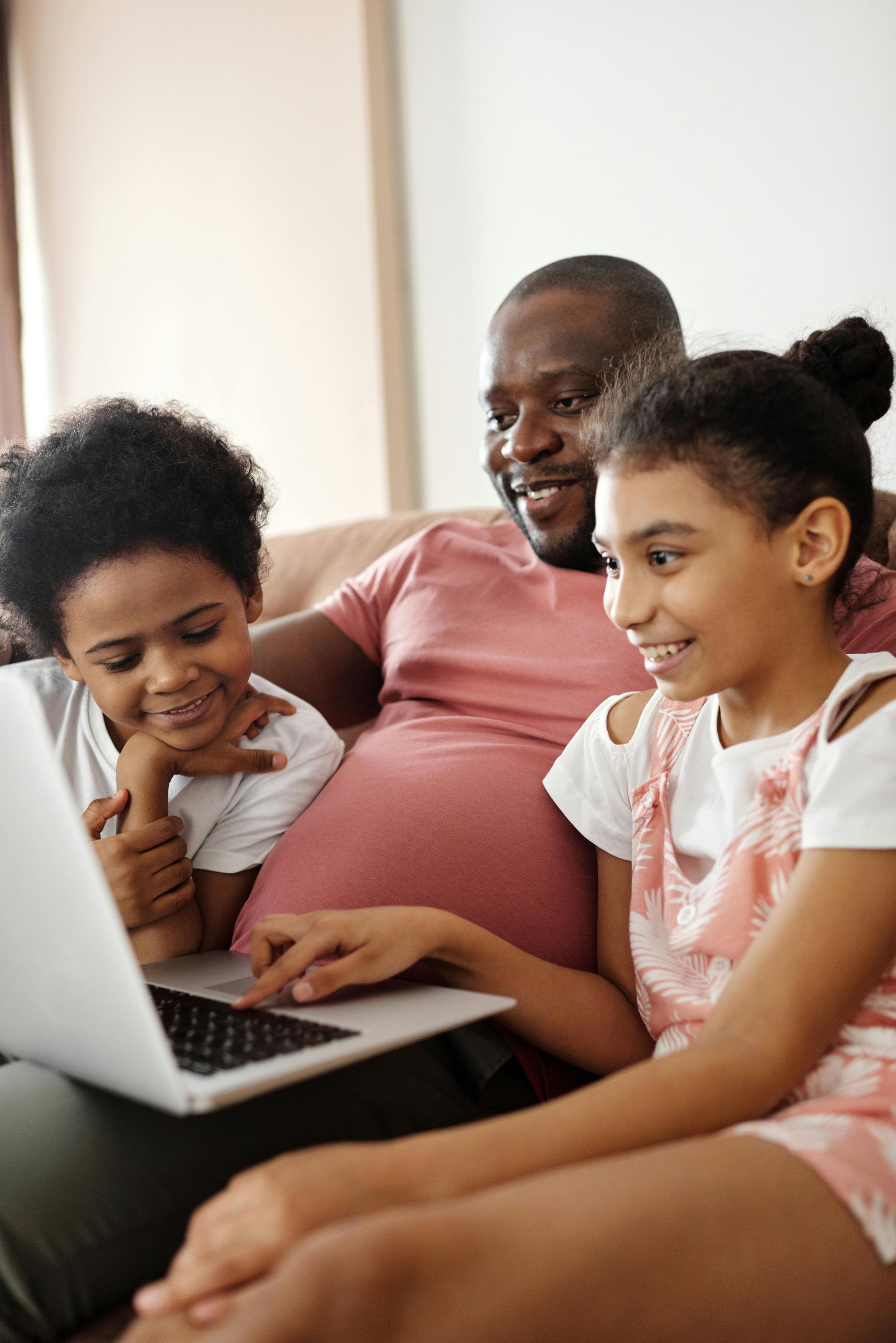 A man and two children are sitting on a couch looking at a laptop.