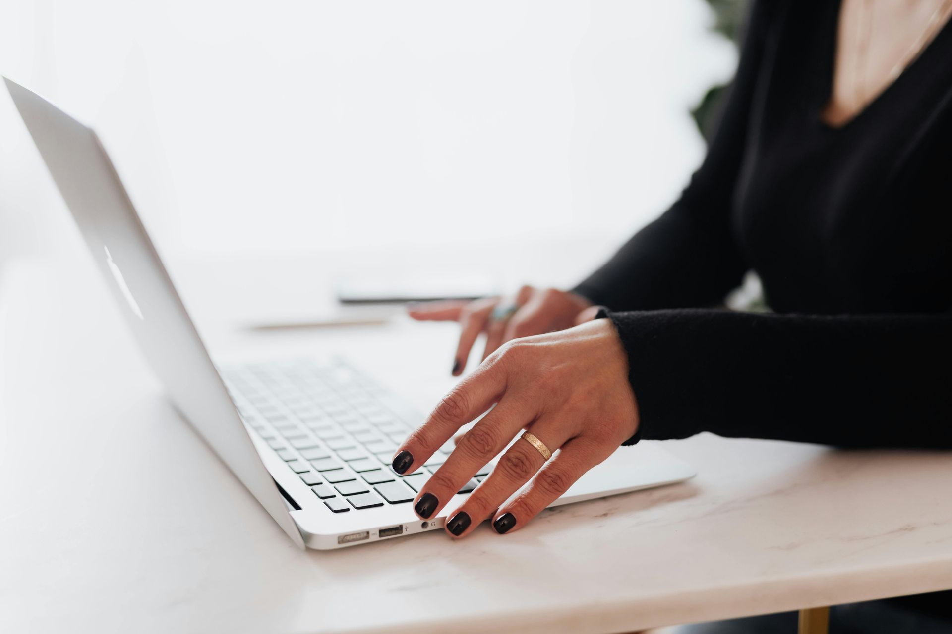 A woman is typing on a laptop computer at a desk.