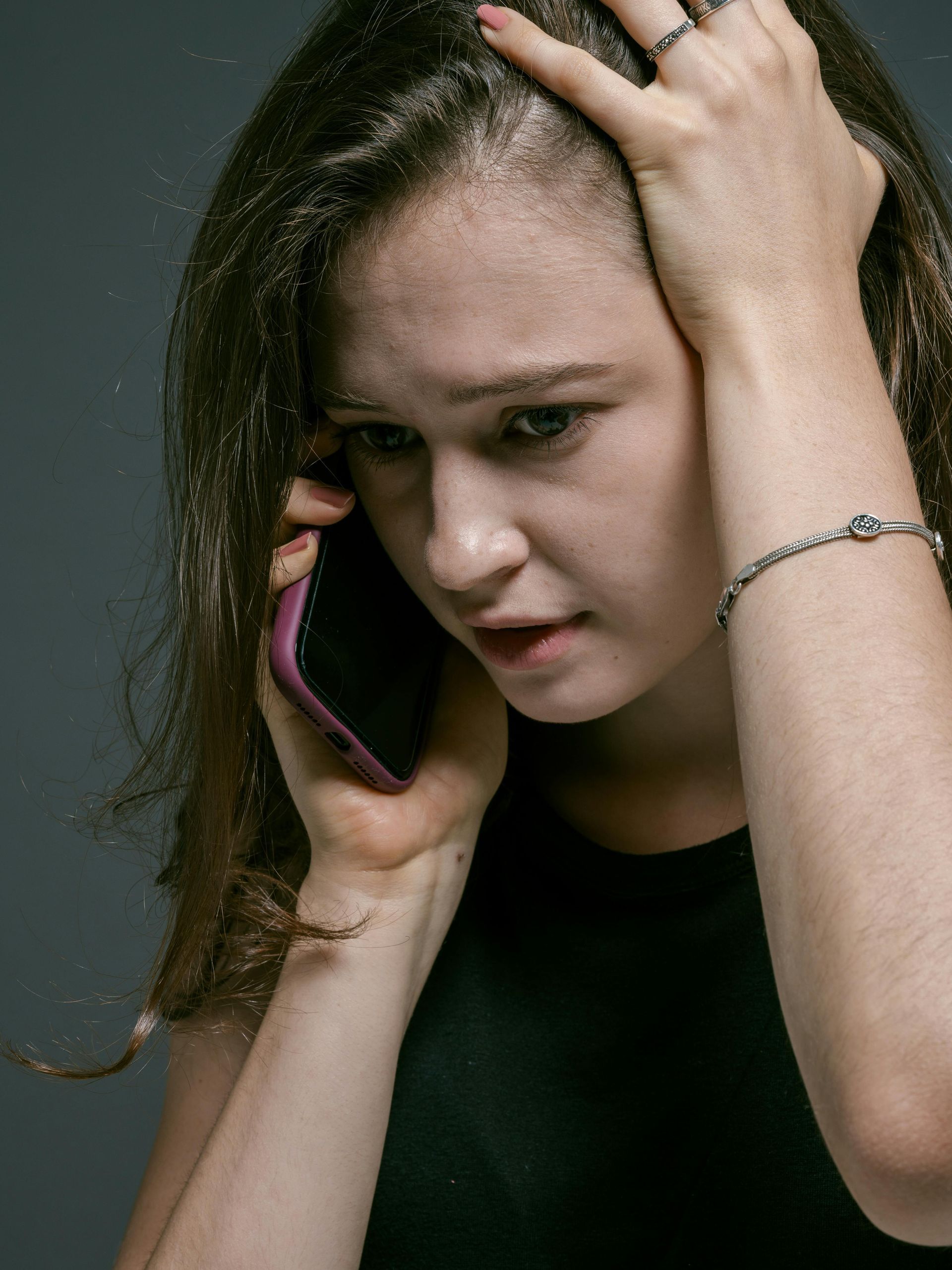 Woman holding a phone to her ear, looking distressed against a dark background.