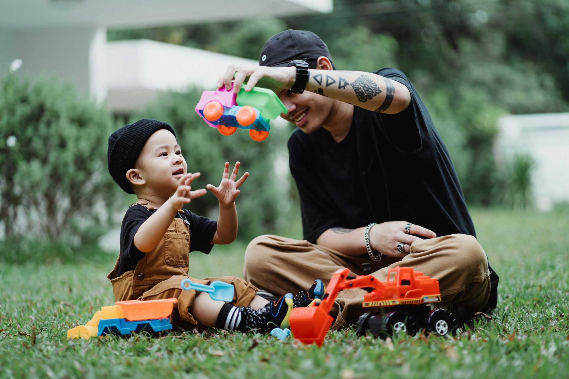 A man and a child are sitting on the grass playing with toys.