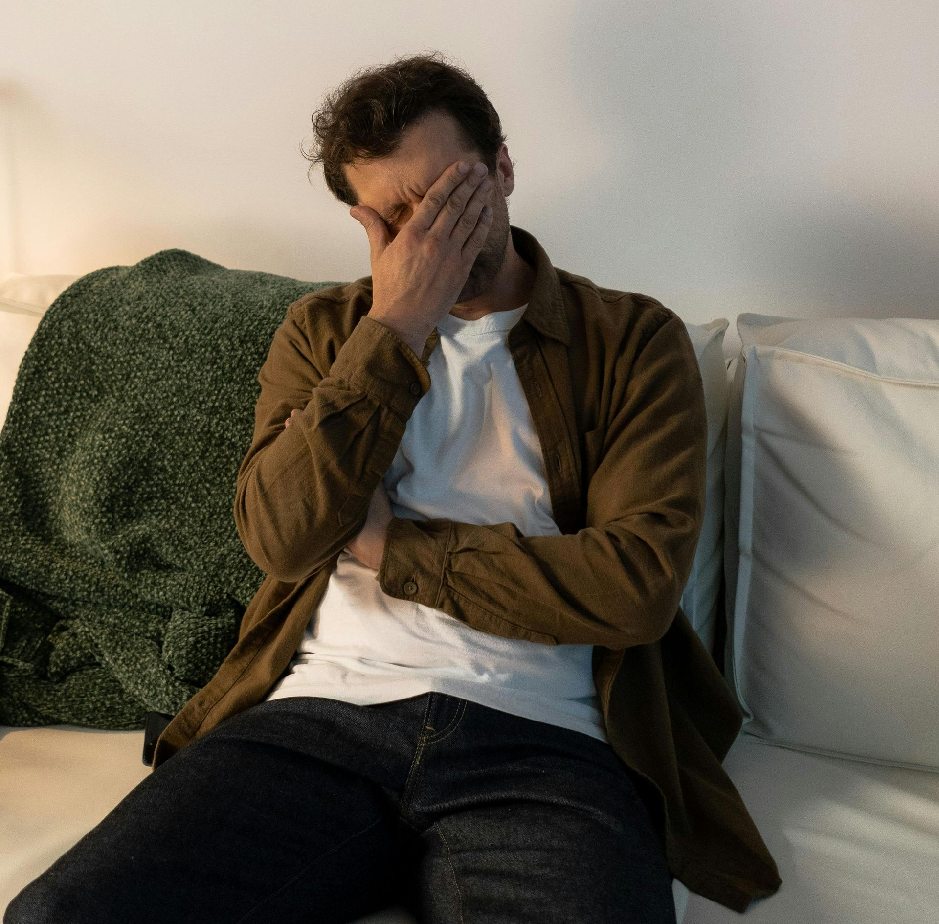 Man sitting on a couch, covering his face with his hand, looking stressed.