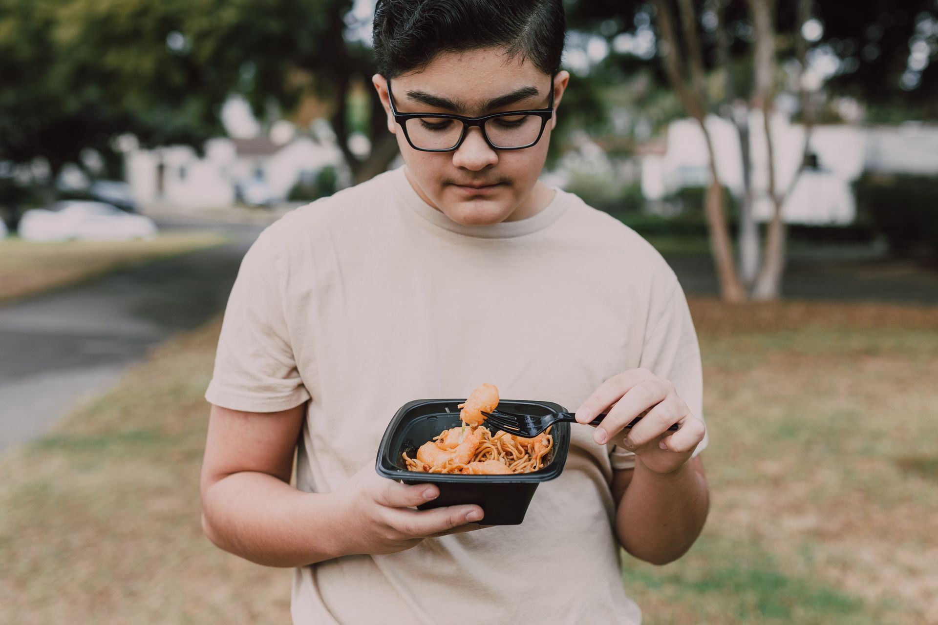 Person outdoors holding a takeout container of fries and a chicken wing