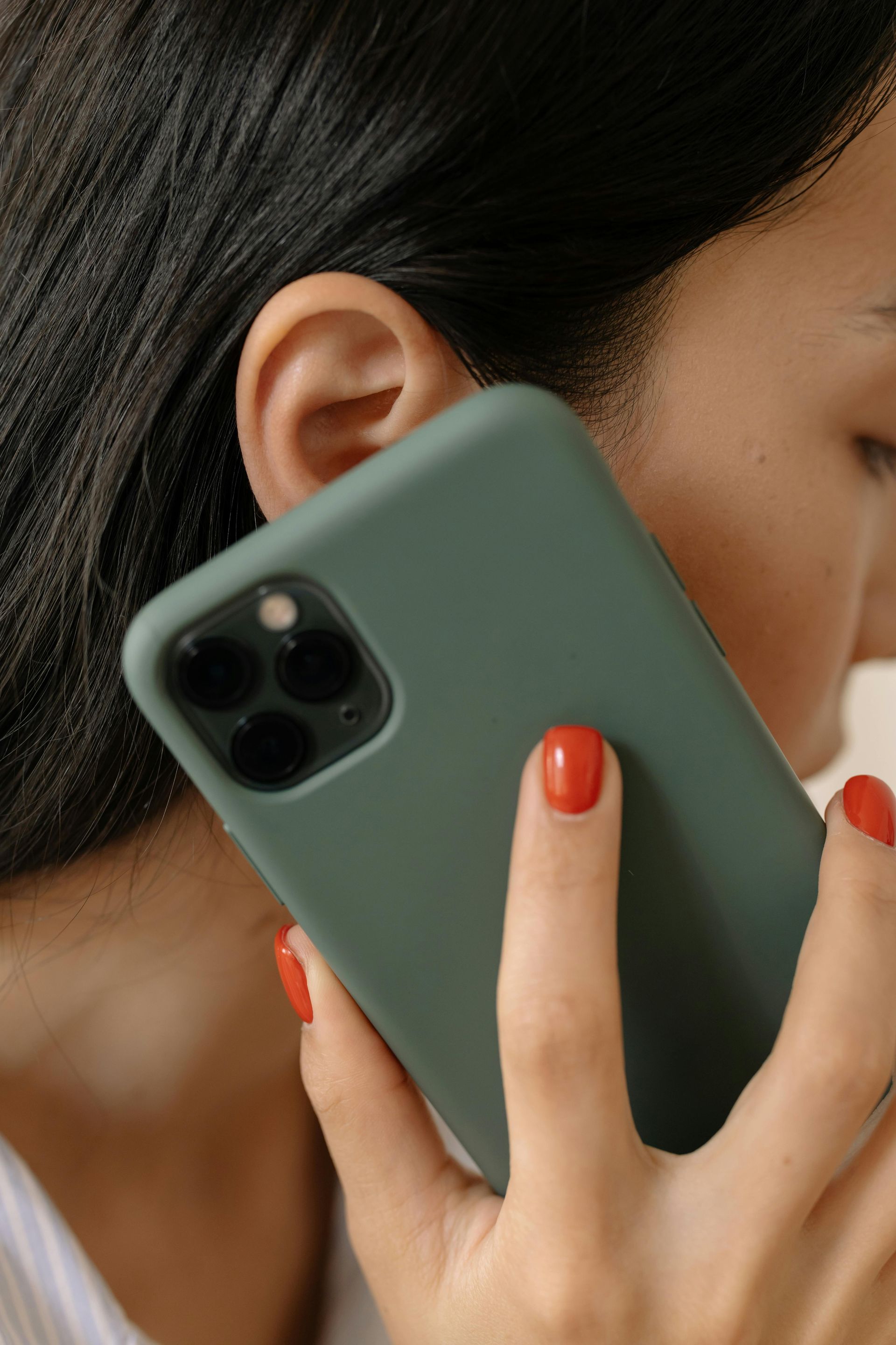 Woman holding a green phone to her ear; red nail polish.