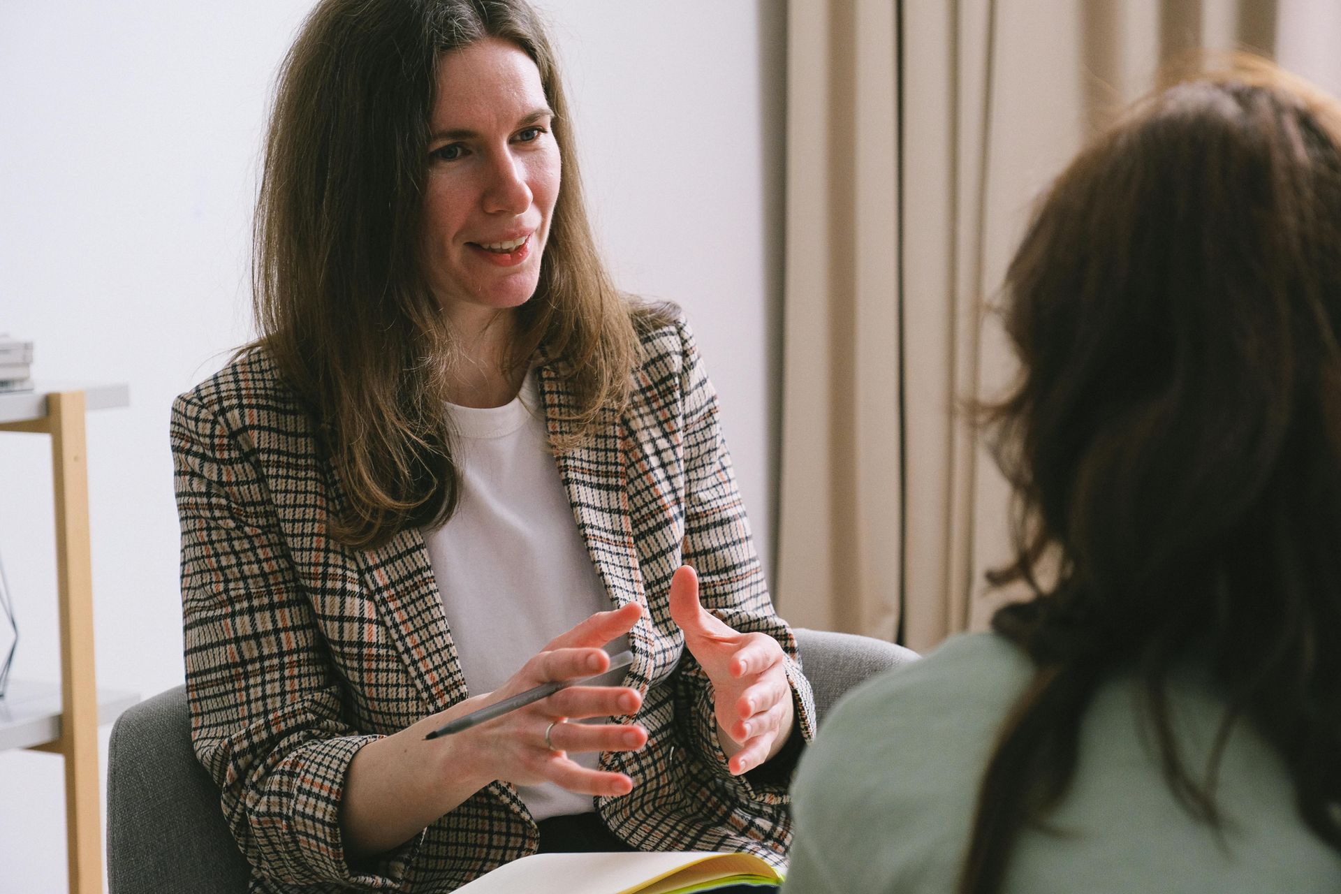 Woman in blazer talking to another woman; counseling session.