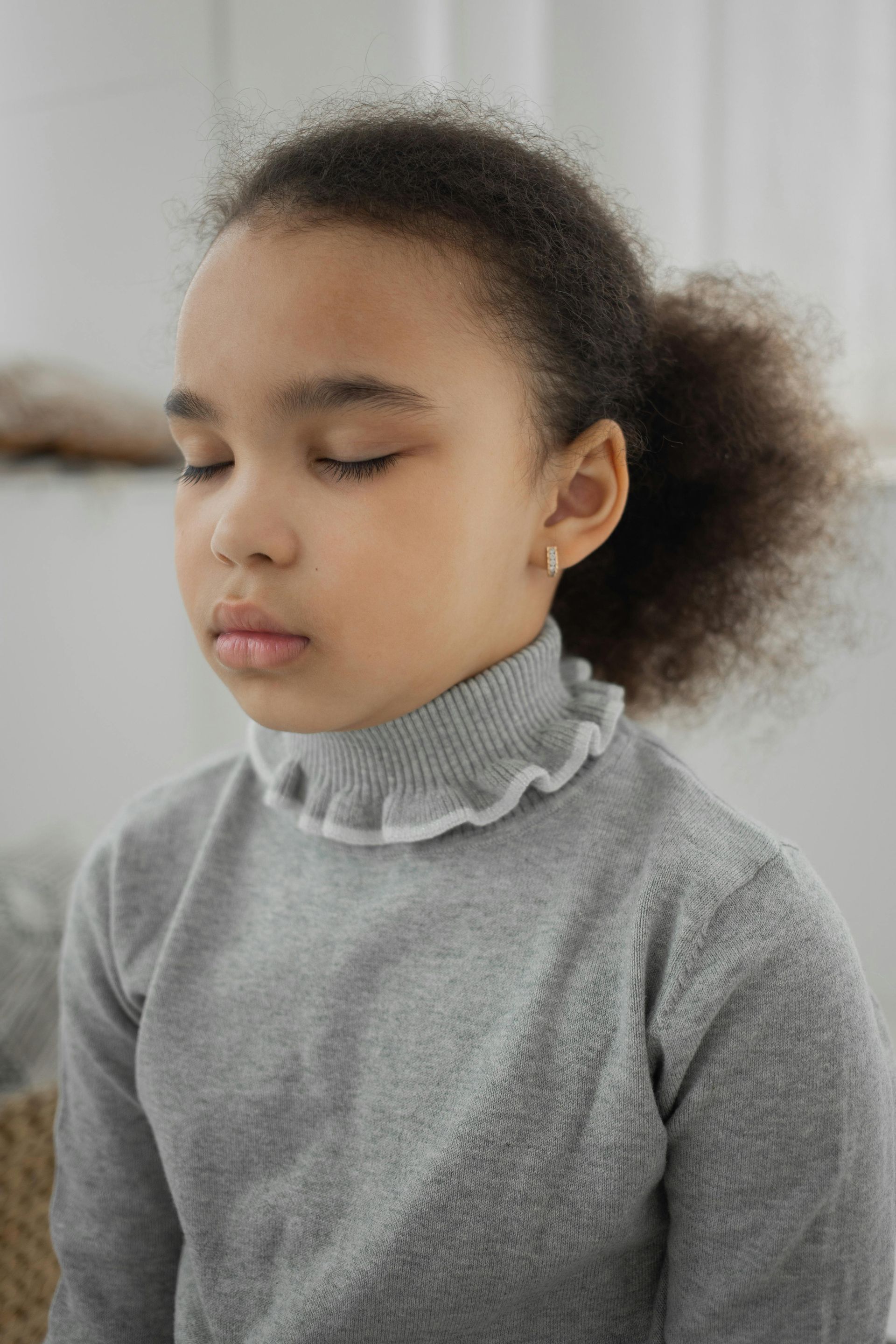 A young girl with closed eyes, wearing a grey turtleneck.