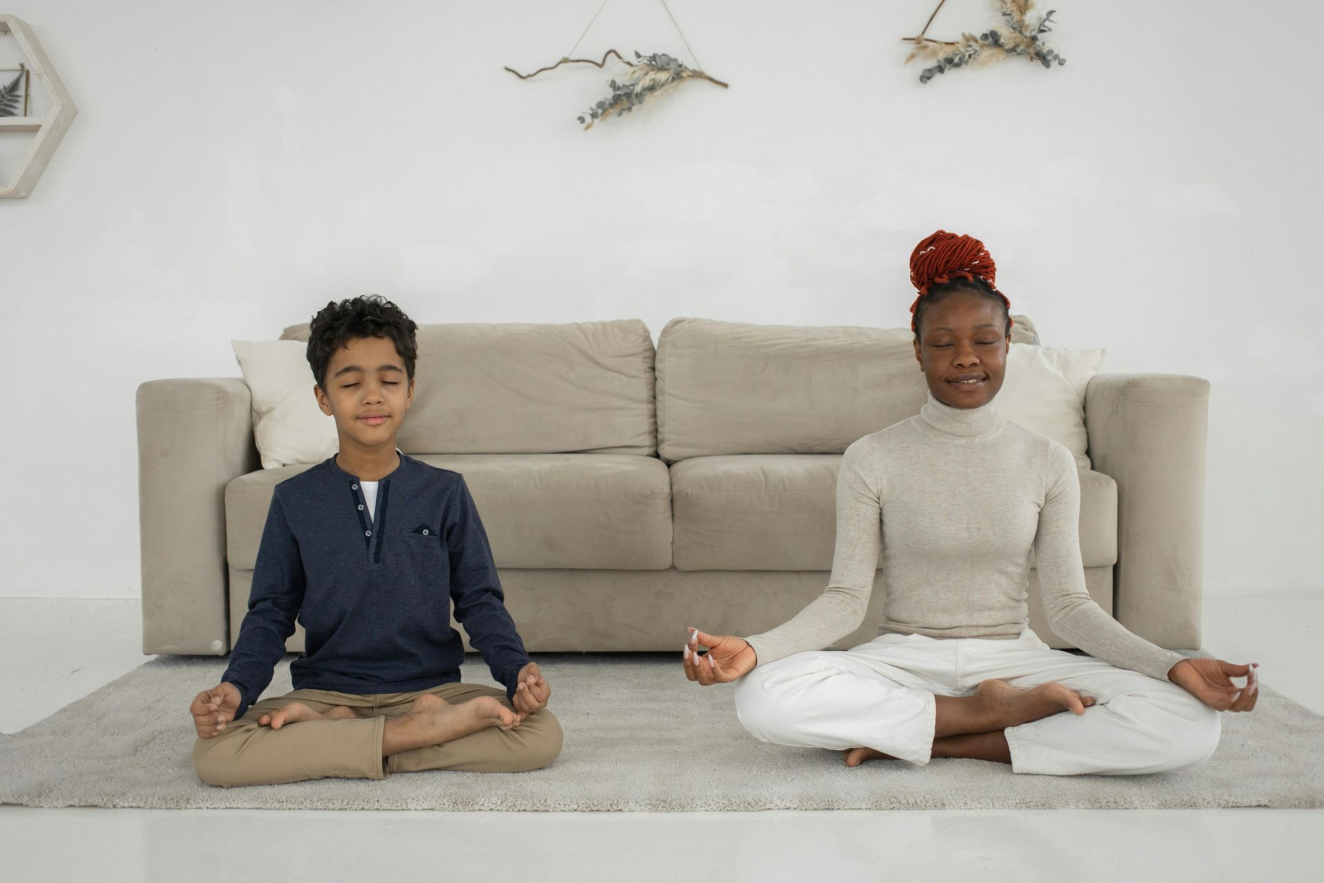 Two people meditating on a rug in front of a sofa. Hands are in a prayer position.
